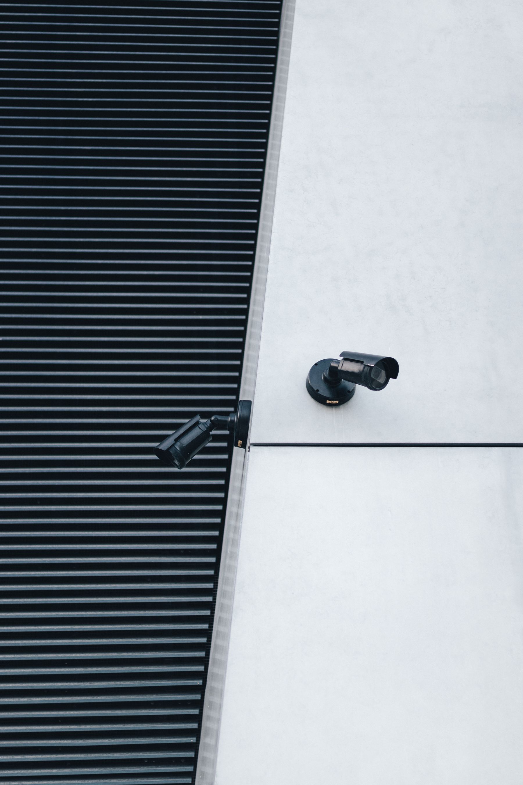 Two exterior security cameras on a commercial building, representing the fixed observation layer around Northline's proposed mobile-sentry service.